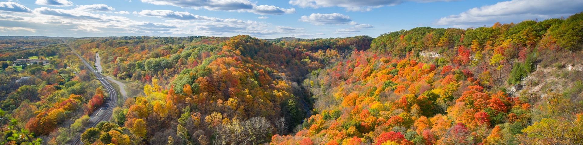 A mountainous landscape with autumn foliage, a winding road, and a clear sky.