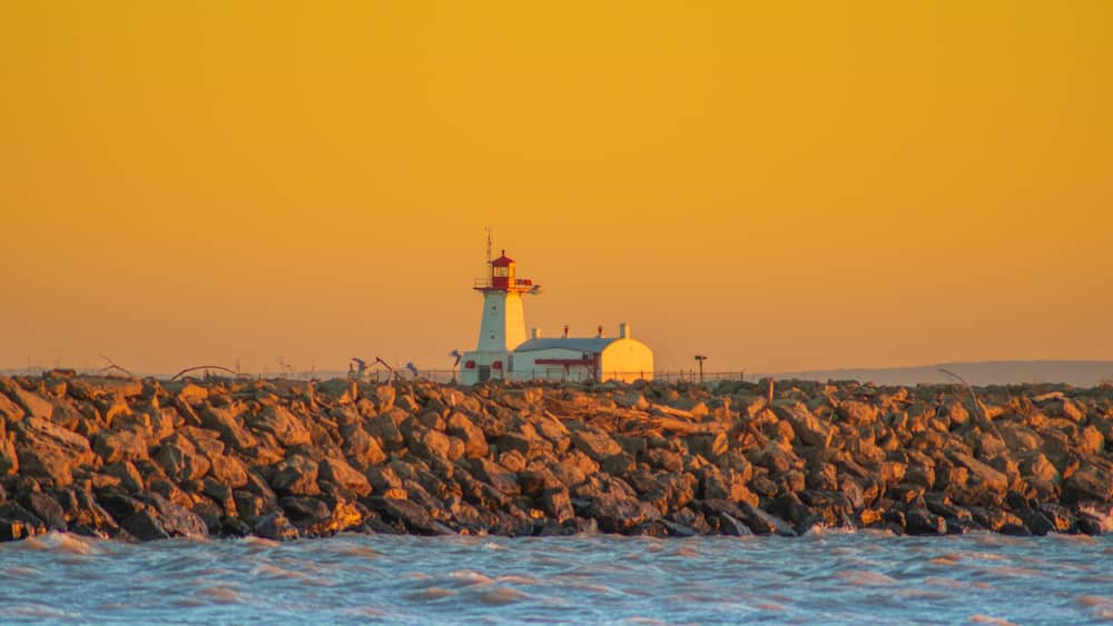 A lighthouse on a rocky shore with the ocean in the foreground.