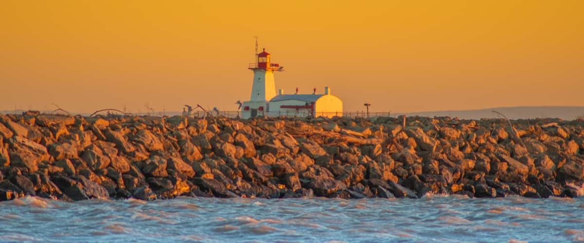 A lighthouse on a rocky shore with the ocean in the foreground.