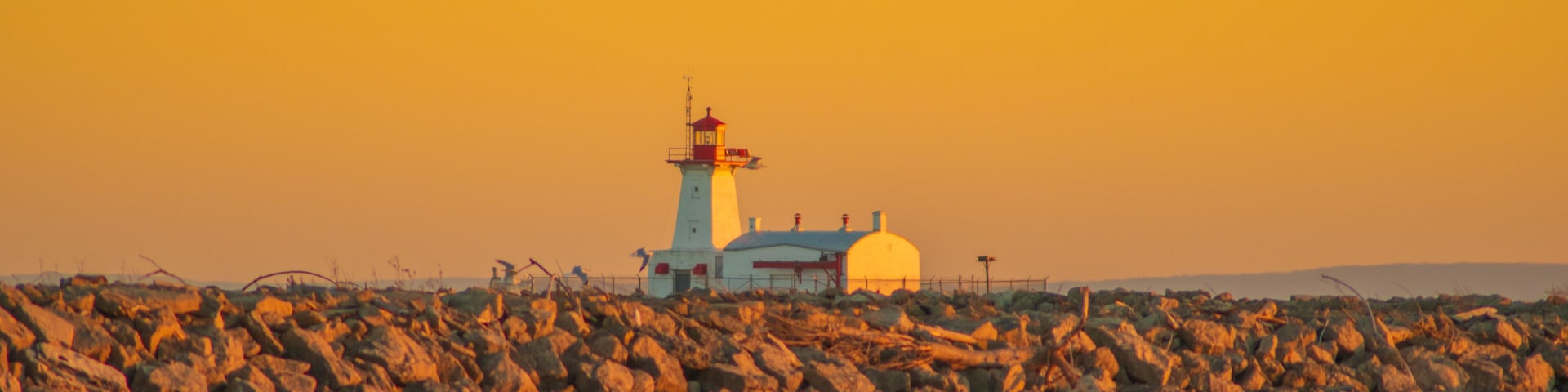A lighthouse on a rocky shore with the ocean in the foreground.
