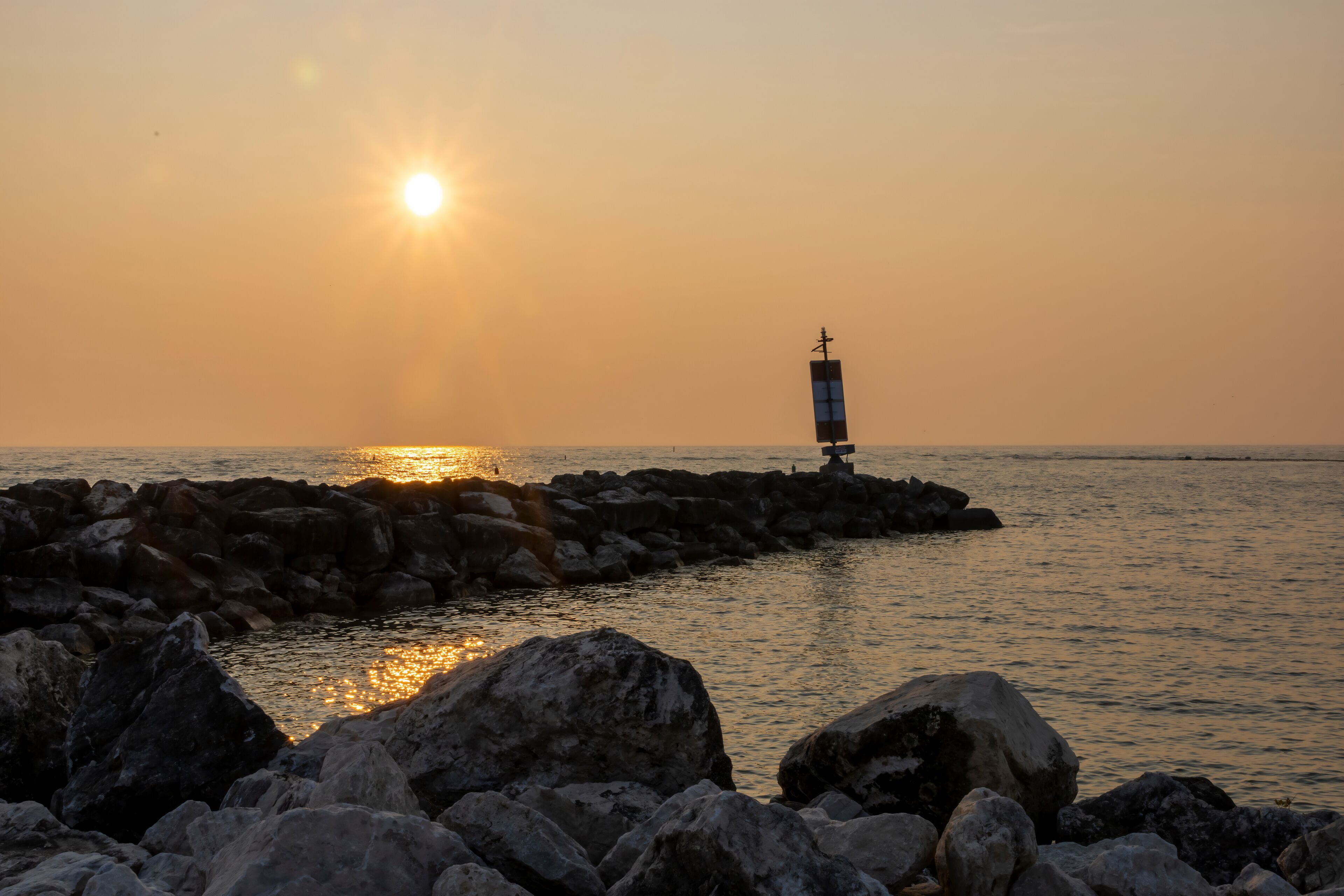 The sun sets over Lake Huron in Port Elgin, Ontario with one of the beach's breakwaters in the foreground.