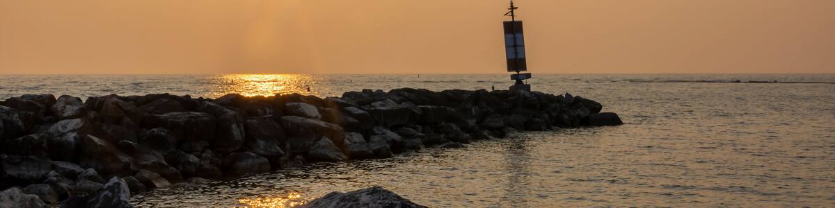 Un coucher de soleil sur une côte rocheuse, avec un phare visible au loin.