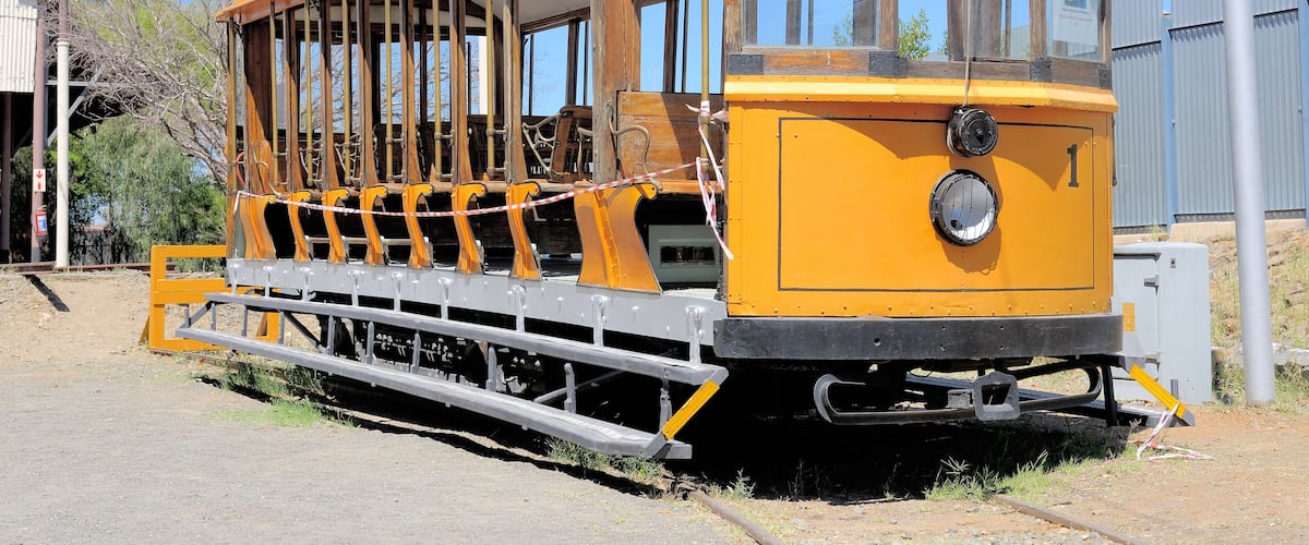 A yellow tram with a glass canopy, wooden seats, and metal tracks.
