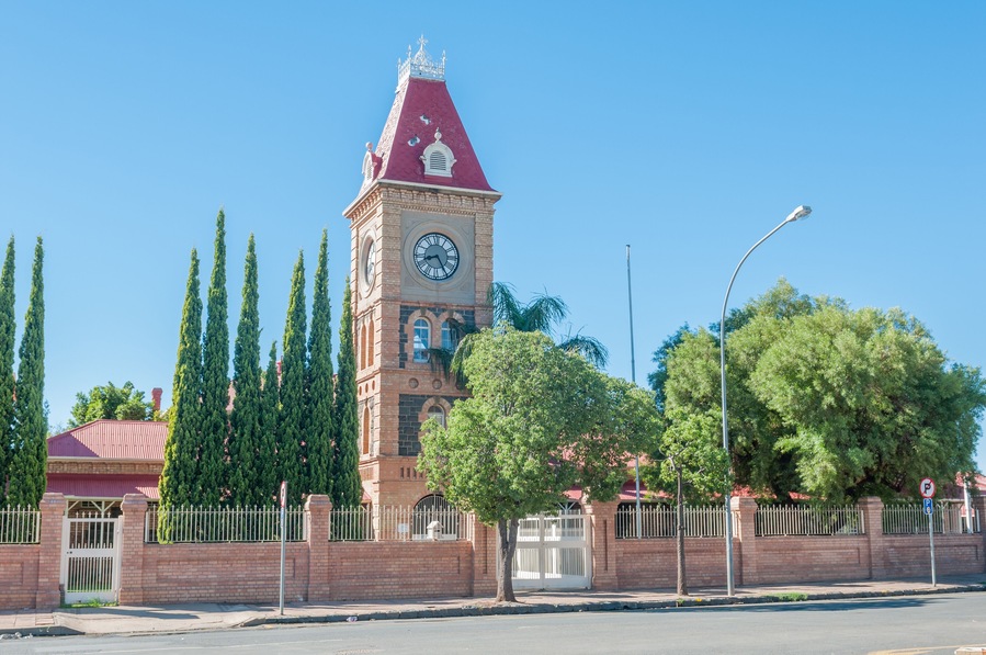 A clock tower with a red roof, surrounded by tall trees and a brick wall.