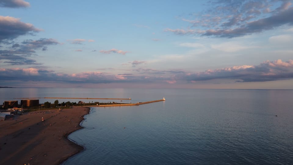 A coastal landscape with a pier extending into the water, a sandy beach, and industrial buildings in the background.