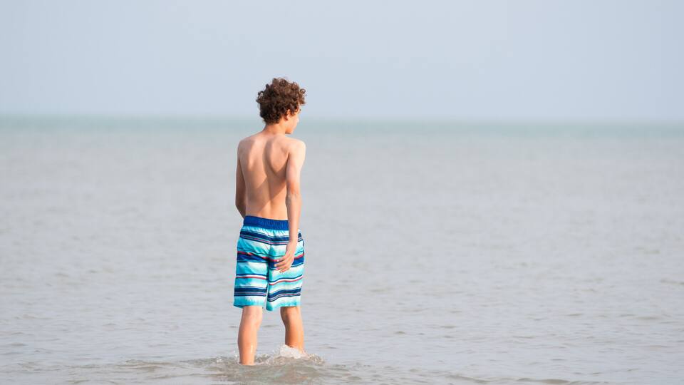 A person standing in shallow water at the beach.