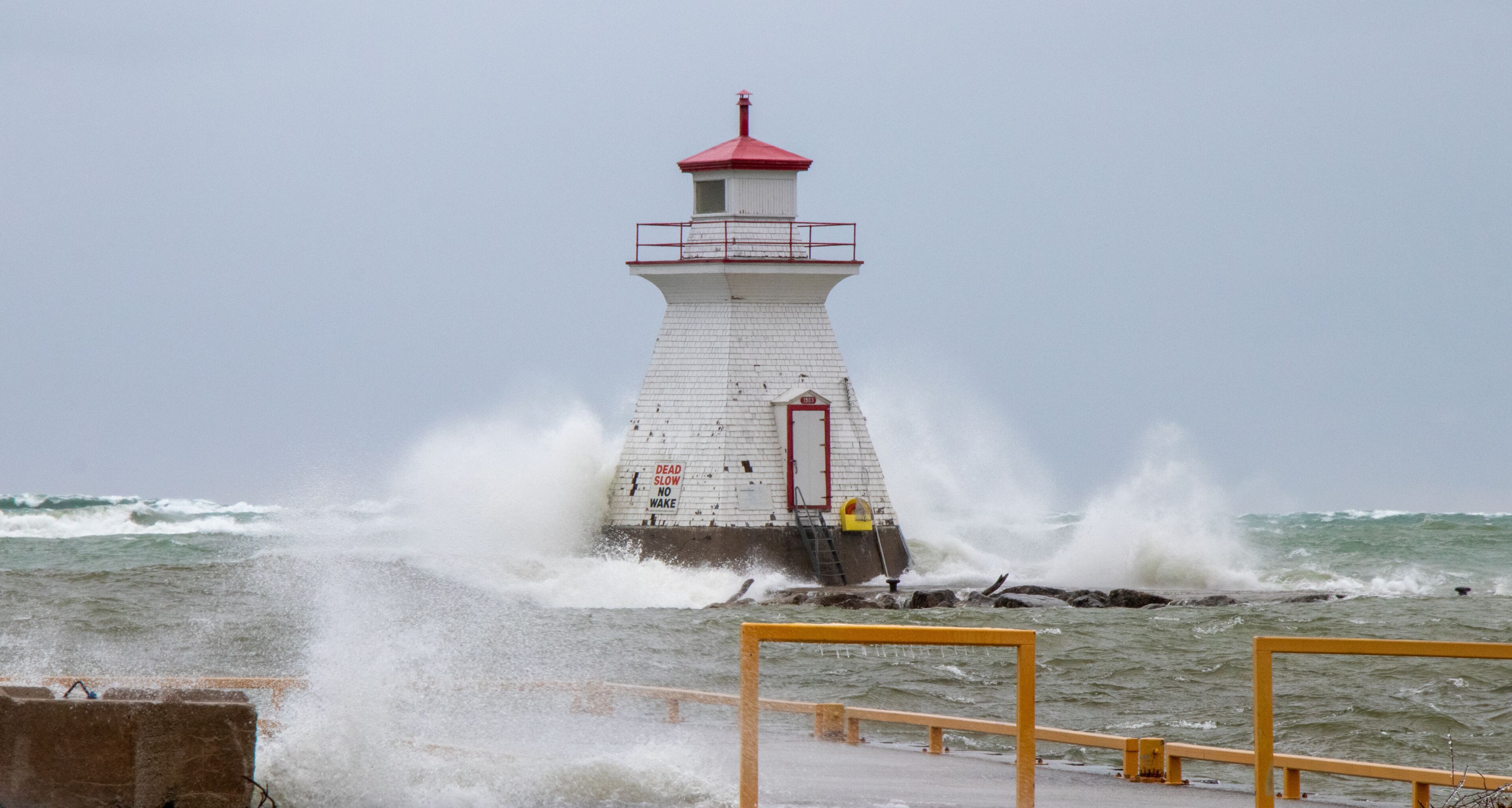 A lighthouse with a red top, surrounded by rough sea waves crashing against it.