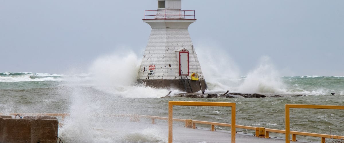A lighthouse with a red top, surrounded by rough sea waves crashing against it.