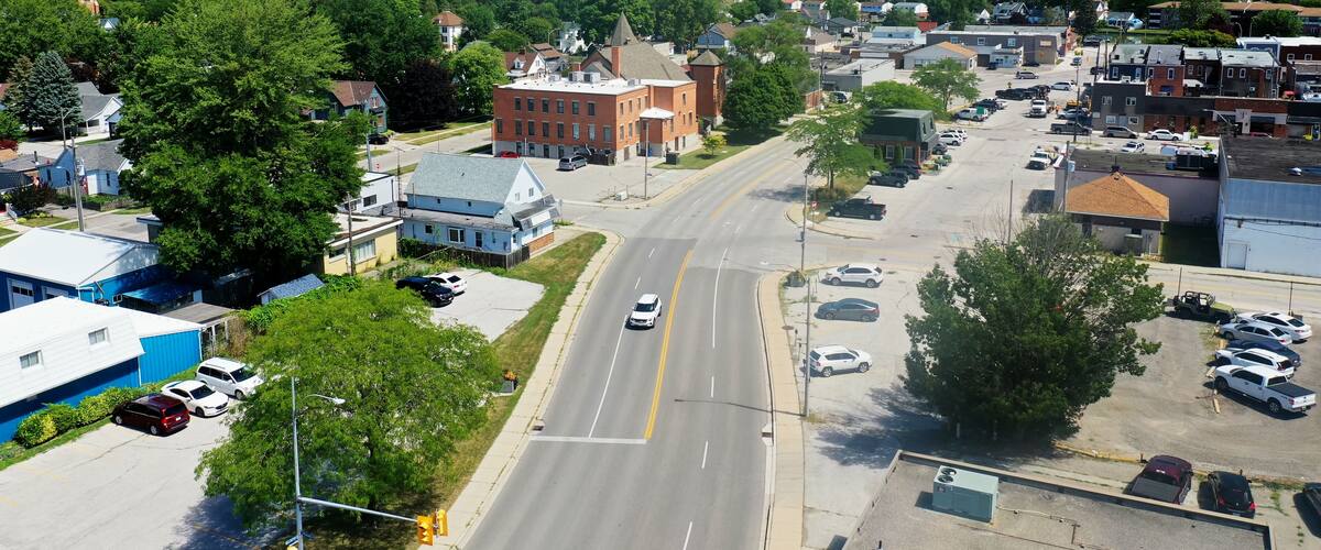 A town with a prominent church steeple, a large brick building, and a wide road with cars.