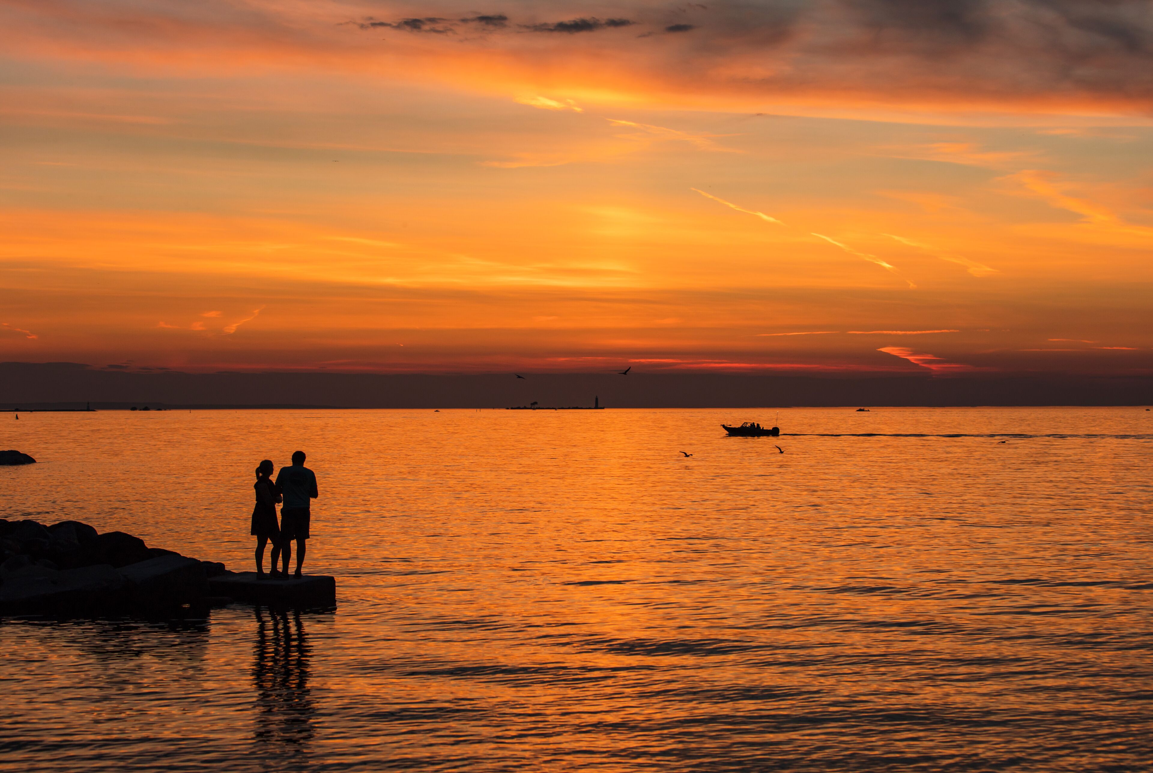A sunset over a calm sea with two silhouetted figures on a dock.