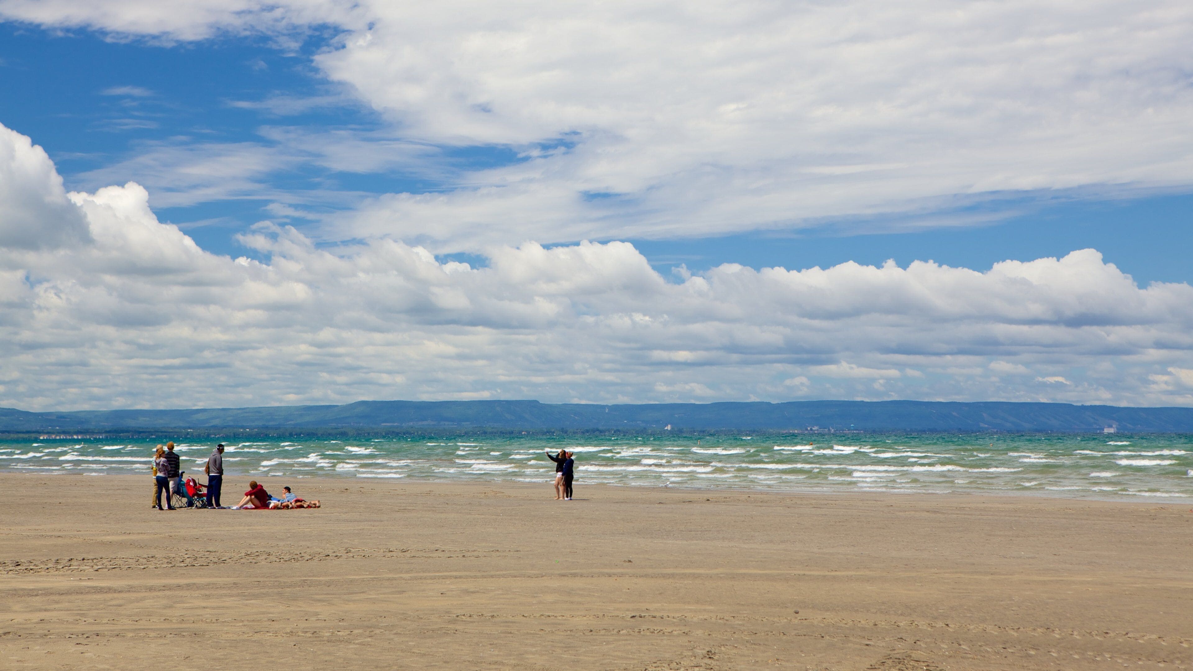 A beach with people, waves, and a cloudy sky.