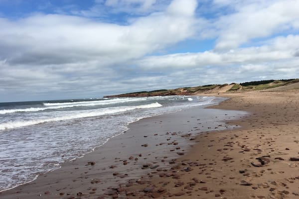 A sandy beach with scattered rocks and waves crashing onto the shore.