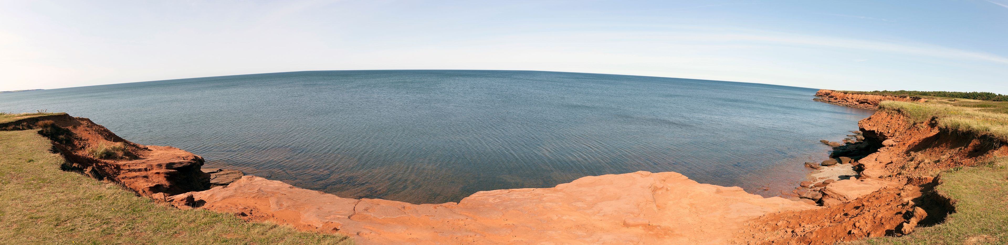 A coastal landscape with a large body of water, red cliffs, and sparse vegetation.