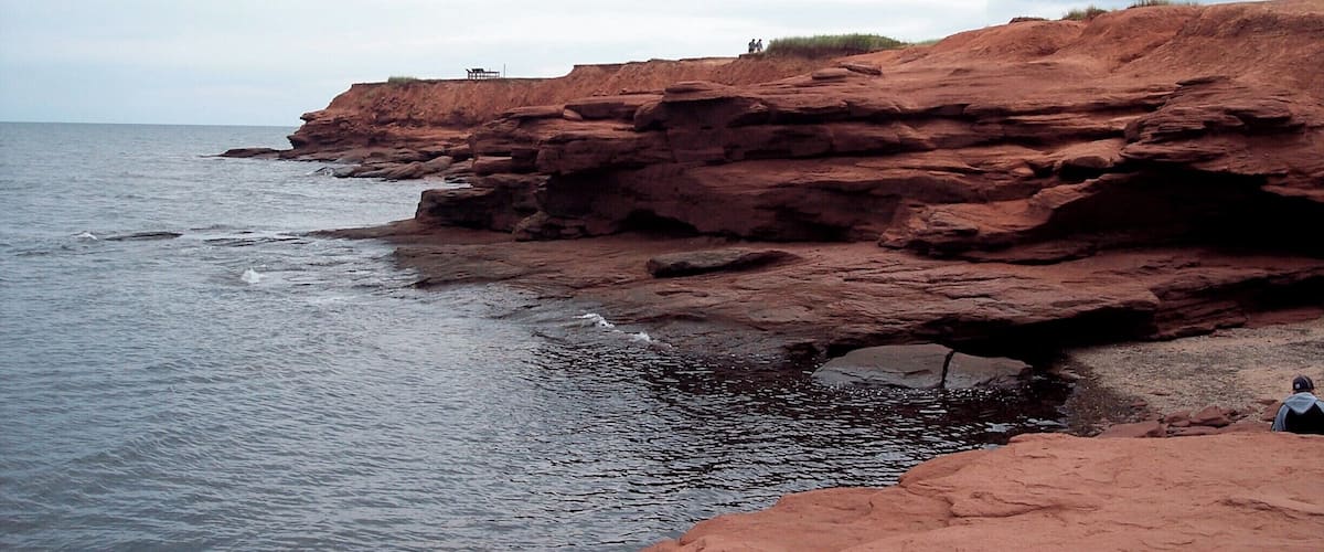 A rocky coastline with a small boat near the shore and a person sitting on the rocks.