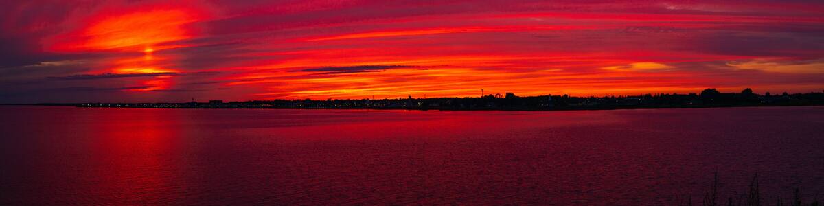 A sunset over a calm body of water with a city skyline in silhouette.