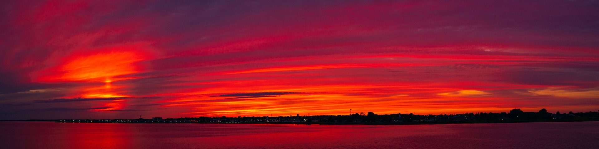 Tramonto su acque calme con la silhouette di uno skyline urbano.
