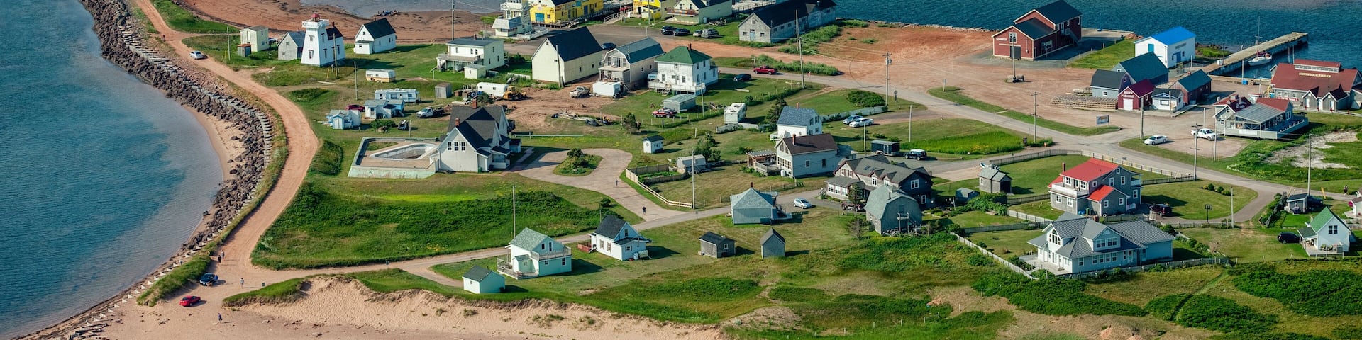 A coastal village with houses, a lighthouse, and a beach.