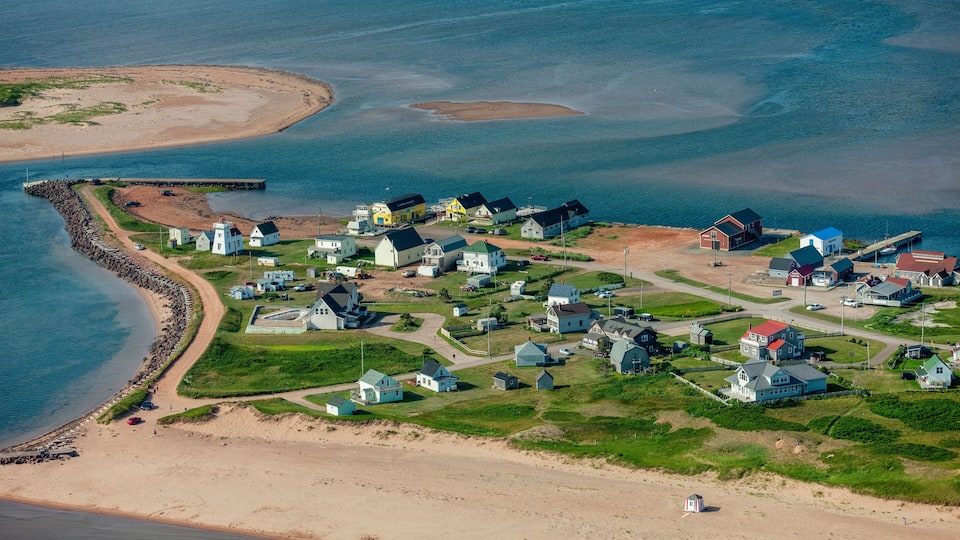 A coastal village with houses, a lighthouse, and a beach.