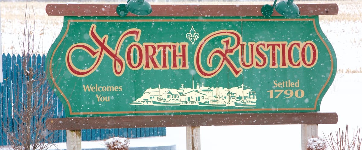 A sign welcoming visitors to North Rustico, established in 1790, with a snowy landscape in the background.
