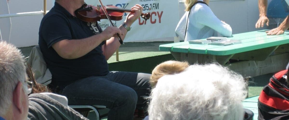 A man playing a violin at an outdoor event with a banner in the background.