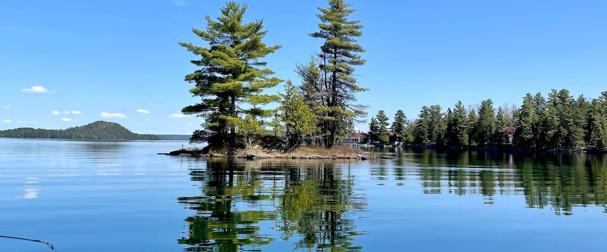 A calm lake with clear reflections of trees and a distant mountain.