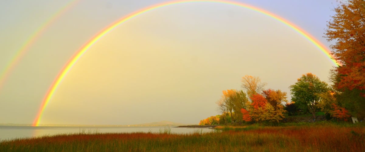 A rainbow over a body of water with autumn trees.