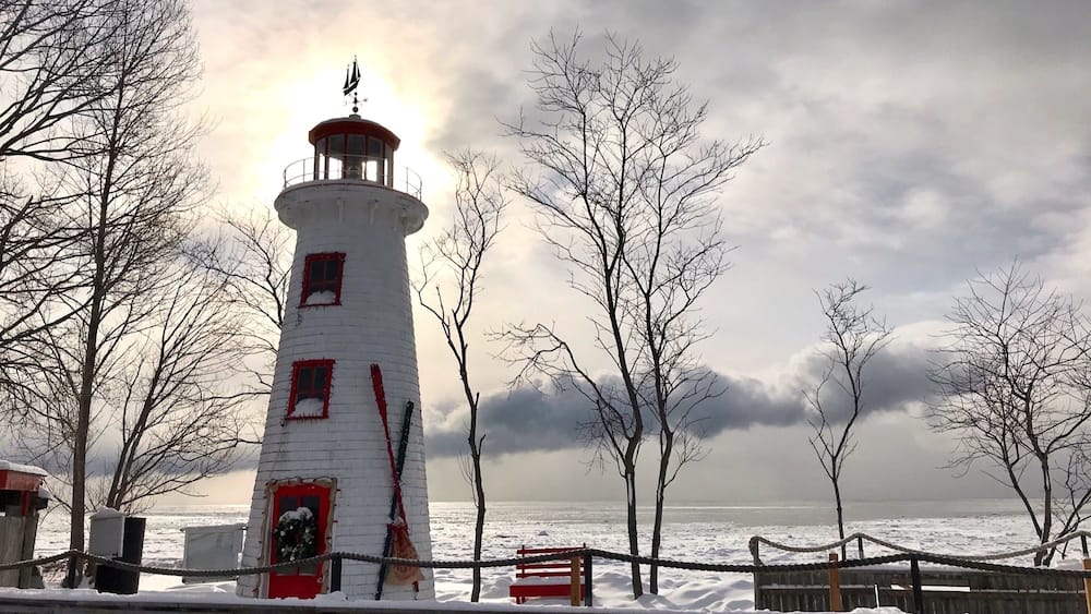 A lighthouse with a red top, surrounded by snow-covered ground and bare trees.