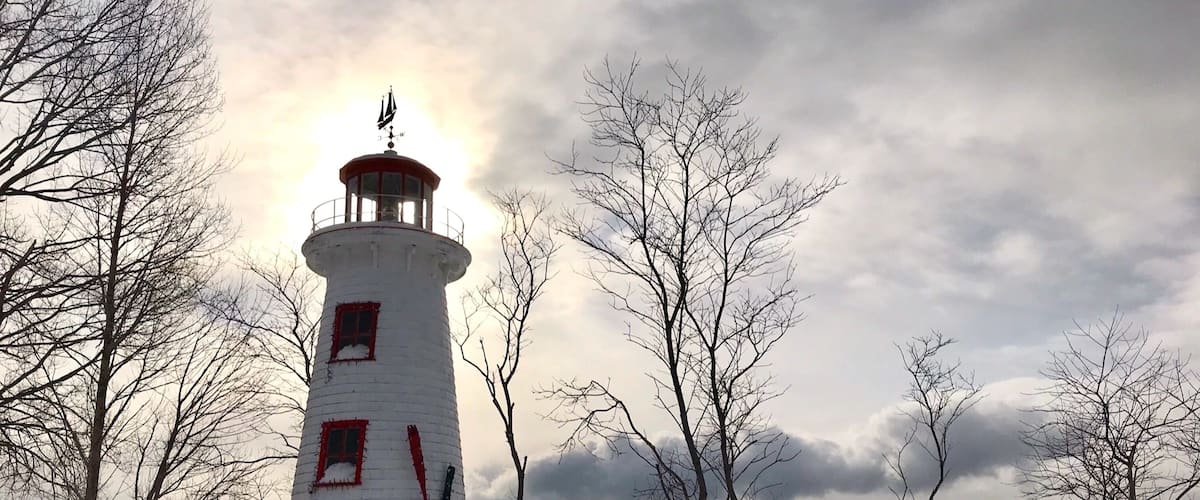 Un phare coiffĂ© dâun dĂŽme rouge, entourĂ© dâun paysage enneigĂ© et dâarbres sans feuilles.