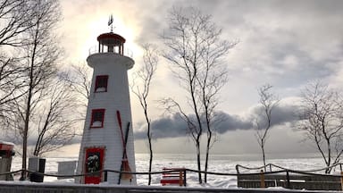 Um farol com a parte superior vermelha, rodeado por terreno coberto de neve e árvores sem folhas.