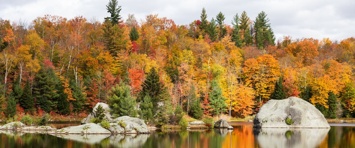 A calm lake reflecting autumn trees and a prominent rock formation.
