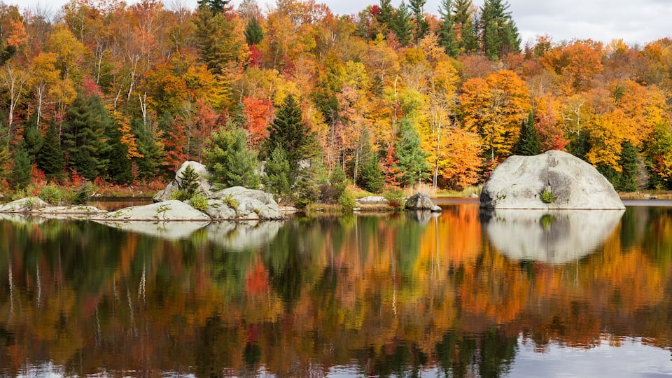 A calm lake reflecting autumn trees and a prominent rock formation.