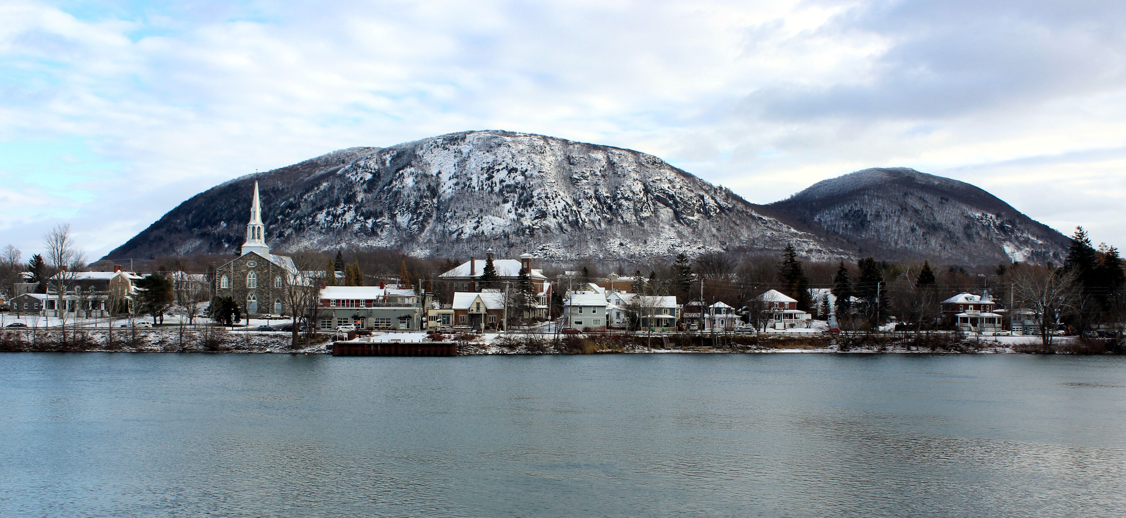 A lakeside town with a church, houses, and snow-covered mountains in the background.