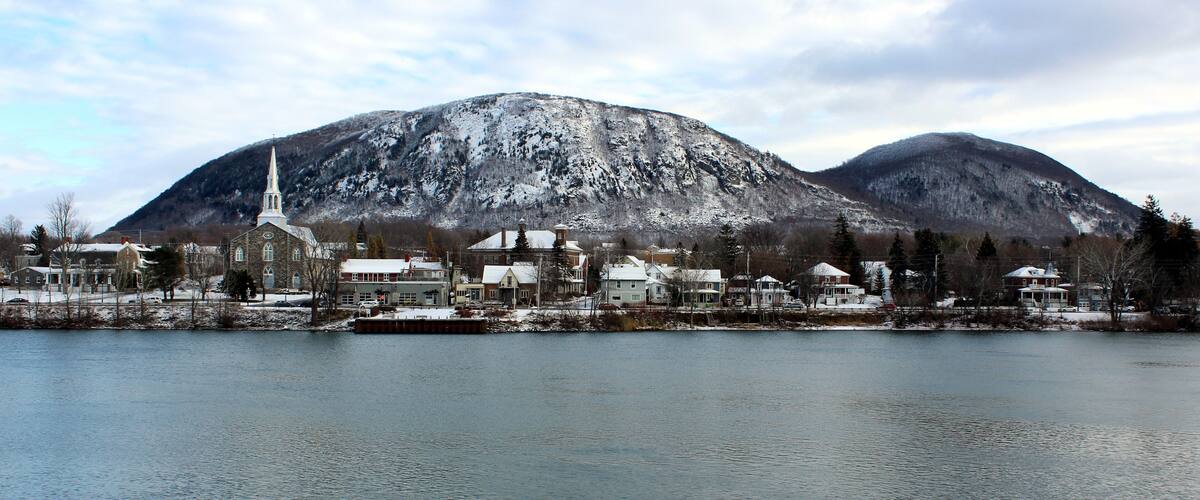 A lakeside town with a church, houses, and snow-covered mountains in the background.