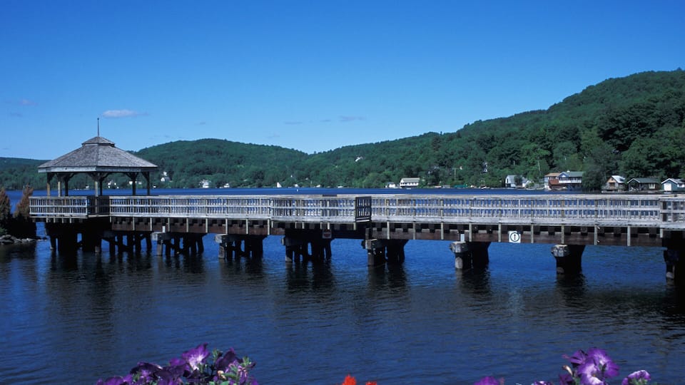 A wooden pier with a gazebo, a bridge, and houses on a hillside.
