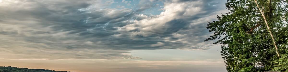 North Hatley, QC, Canada - September 5, 2014: Red, yellow, blue and green kayaks sit on a pebbly beach beside a stand of trees as the sun rises with dramatic clouds over Lake Massawippi