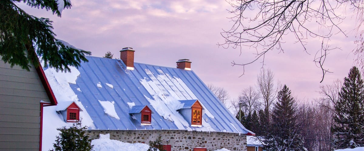 A stone house with a blue roof and red accents, surrounded by snow and trees.