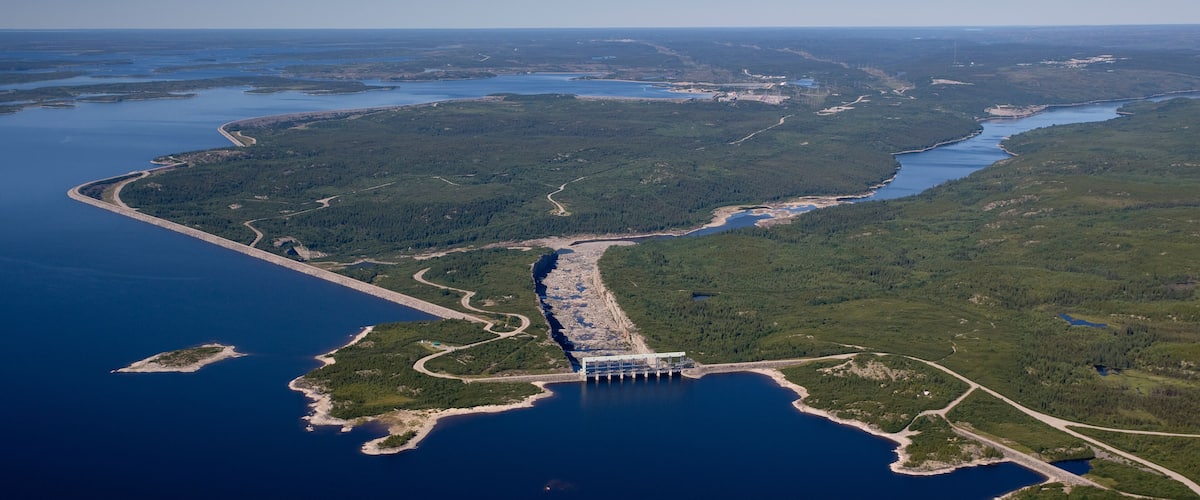 An aerial view of a coastal area with a large body of water, a bridge, and dense forest.
