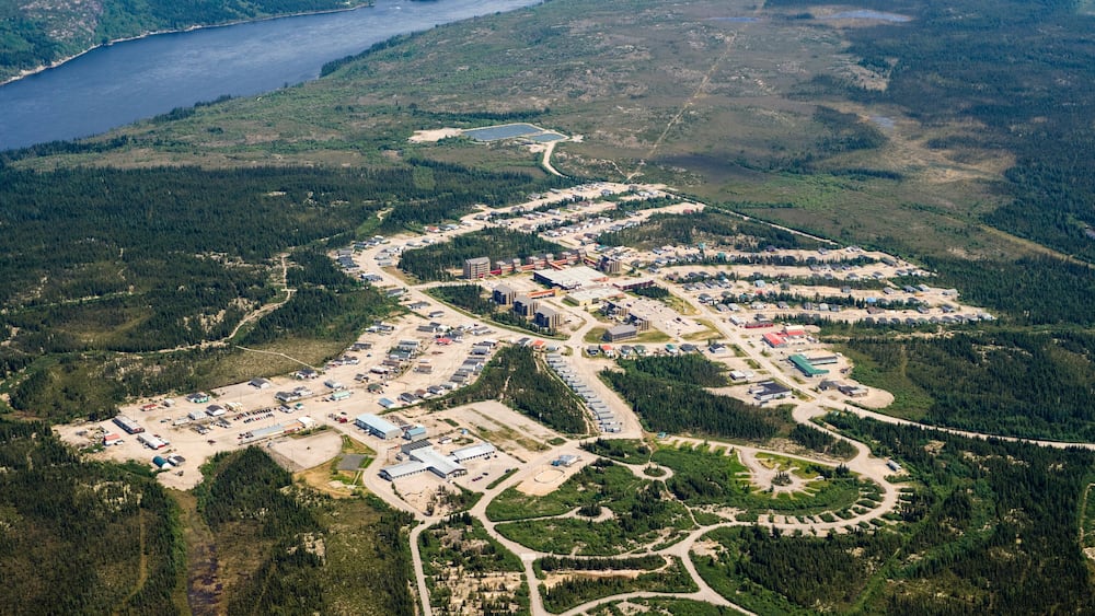Une vue aérienne d’un vaste complexe industriel composé de nombreux bâtiments et de routes, entouré de forêts denses et d’un lac.