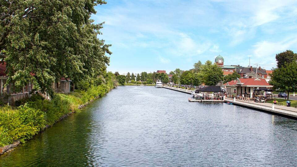 A river with a boat docked on the right, surrounded by greenery and buildings.