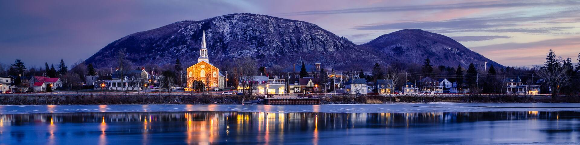 A frozen lake with a church and mountains in the background.