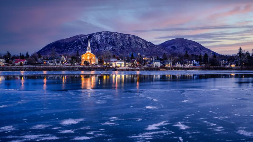 A frozen lake with a church and mountains in the background.