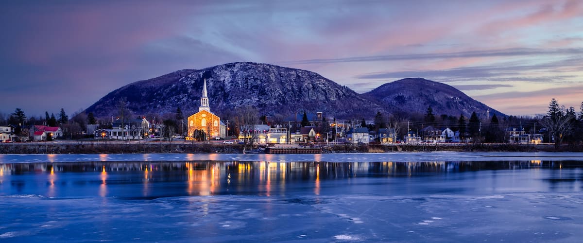 A frozen lake with a church and mountains in the background.