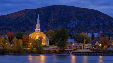 Uma igreja com uma torre, rodeada por árvores de outono e uma montanha ao fundo.
