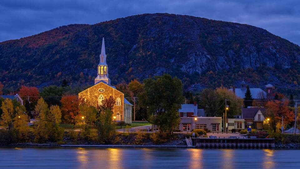 A church with a spire, surrounded by autumn trees and a mountain in the background.