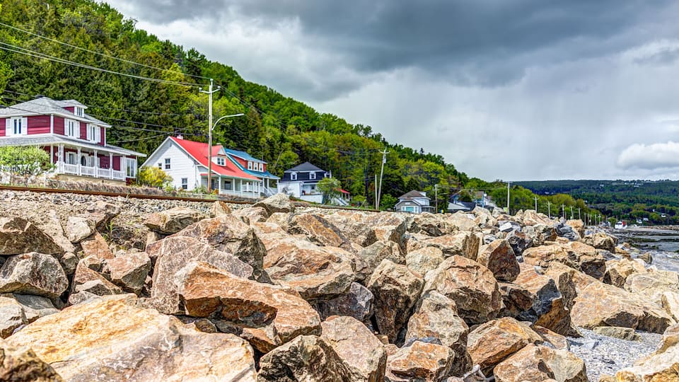 A rocky shoreline with houses and a forested hill in the background.