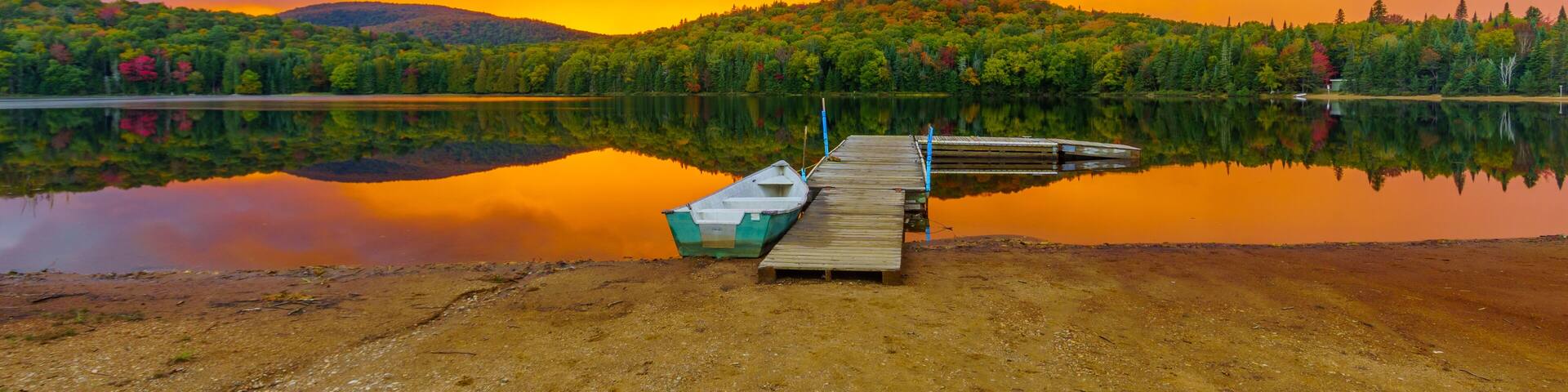 A serene lake with a wooden dock and a small boat, surrounded by lush green trees and a dramatic sunset sky.