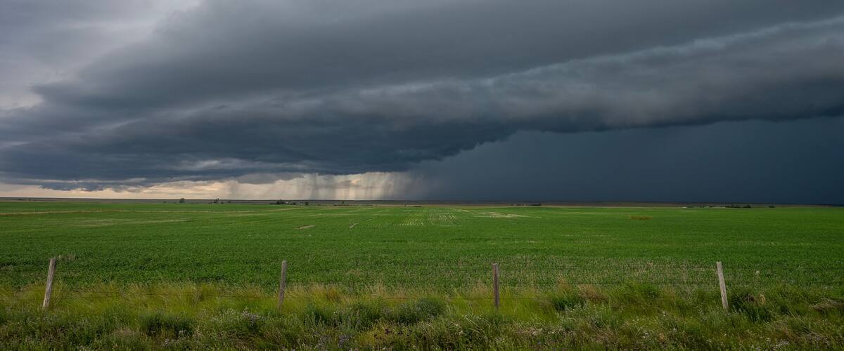 A stormy sky over a green field with a fence in the foreground.