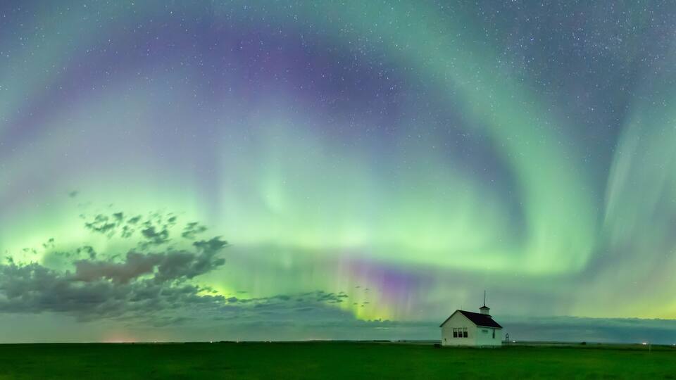 A white house with a green field and the Northern Lights in the sky.