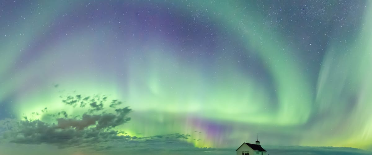 A white house with a green field and the Northern Lights in the sky.