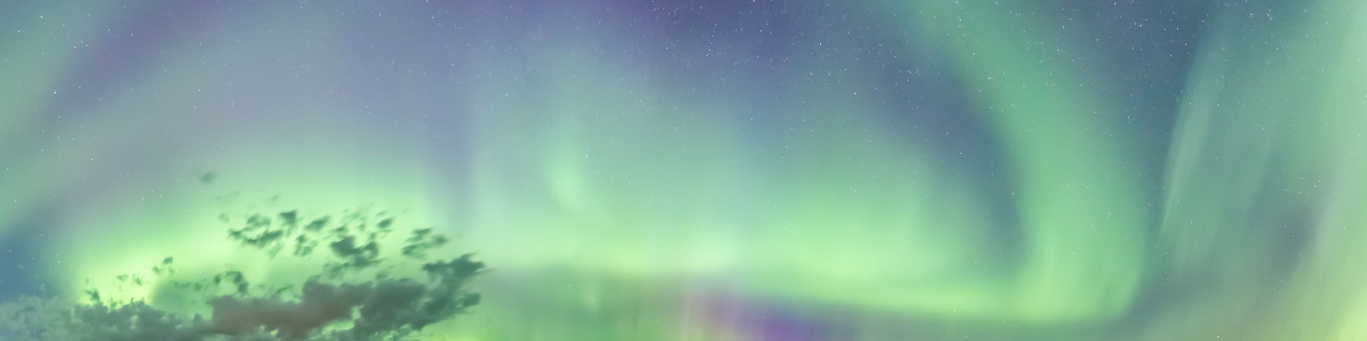 A white house with a green field and the Northern Lights in the sky.